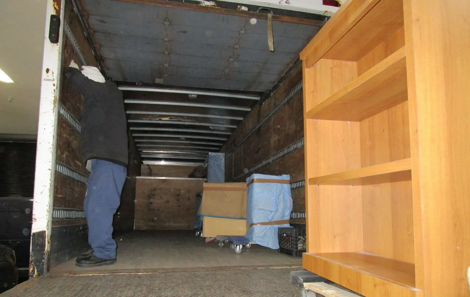 Person loading a moving truck with furniture and boxes, viewed from inside the cargo area