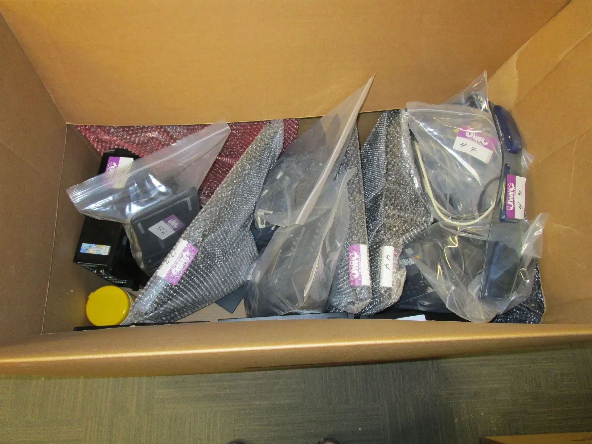 Open cardboard box filled with assorted small packaged electronics accessories and cables