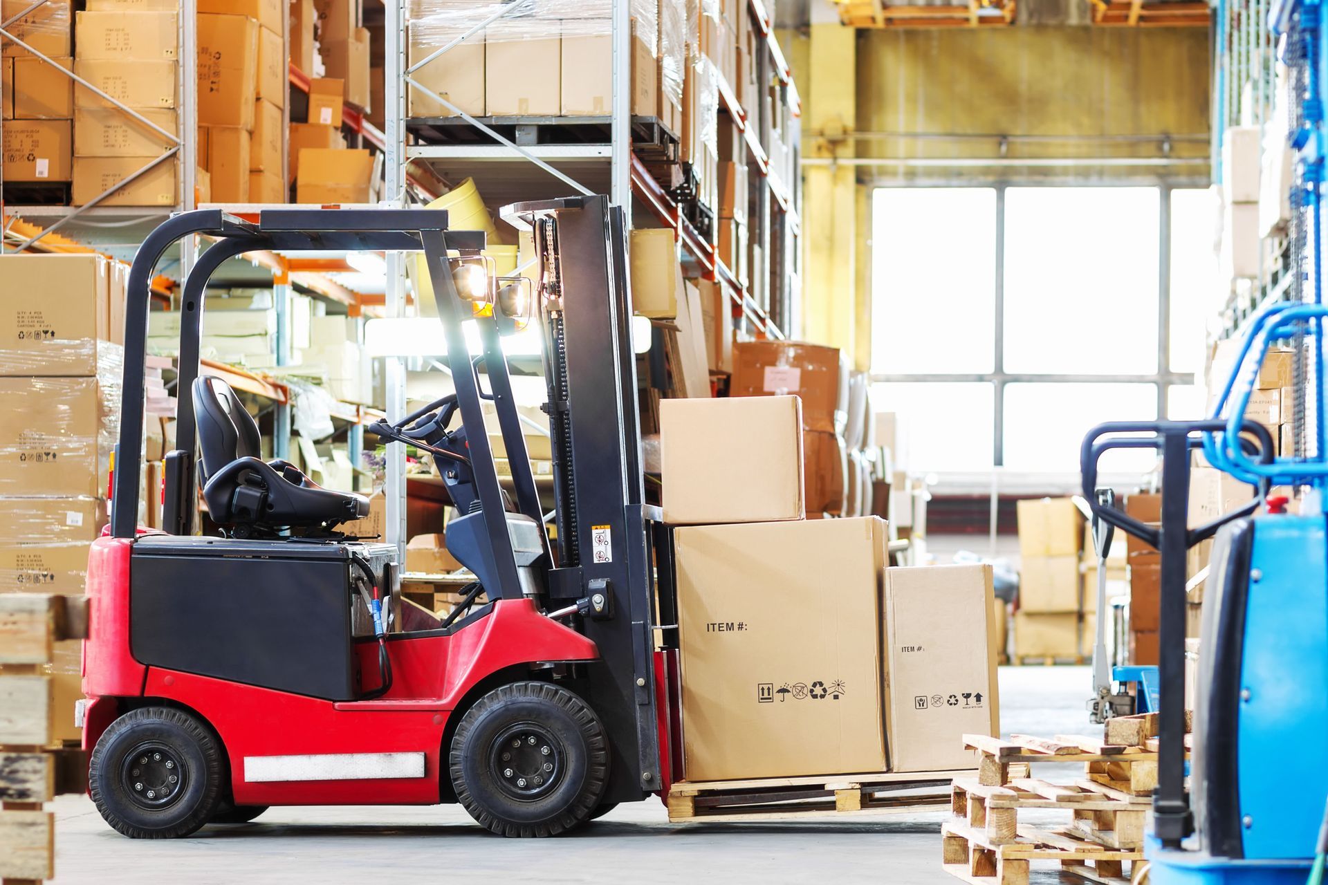 Red forklift in a warehouse beside stacked boxes and pallets