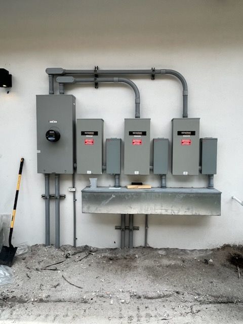 Outdoor electrical panel with meter, three circuit breaker boxes, mounted on a wall, gray conduit, and a shovel.