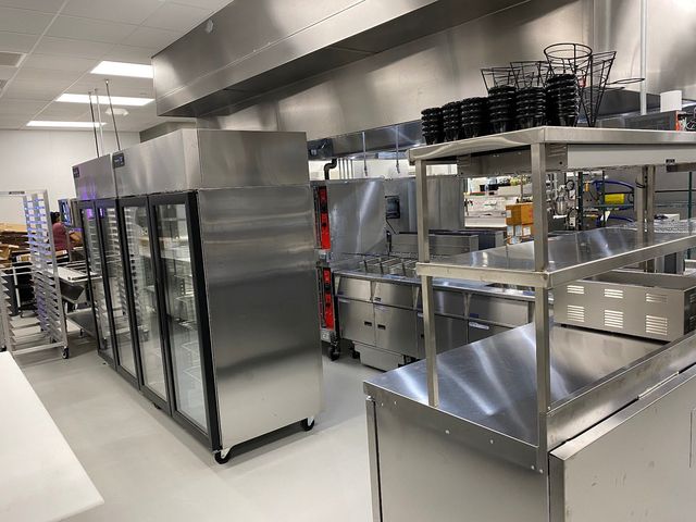 Stainless steel commercial kitchen with shelves, refrigerators, and prep counters under bright lights