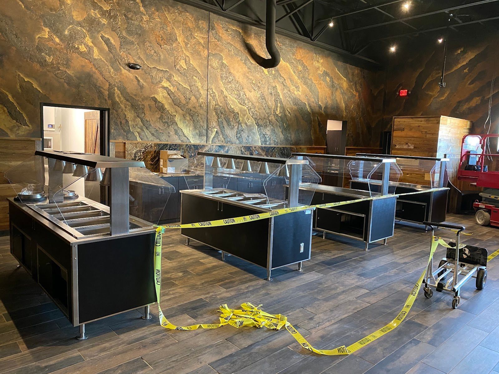 Empty buffet station with metal counters and caution tape in a dim restaurant dining room