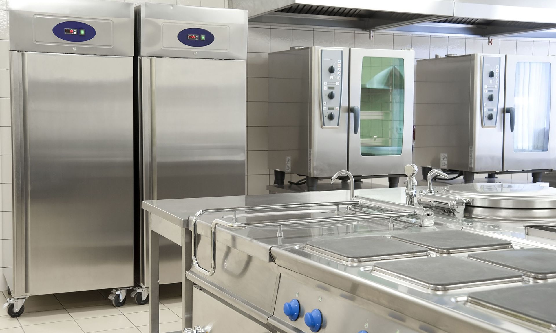 Stainless steel commercial kitchen with ovens, prep tables, and refrigerators.
