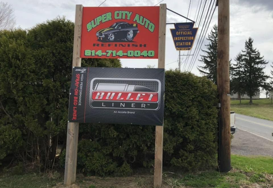 Roadside sign for Super City Auto and KULLER INC., with phone number, beside trees and a road.