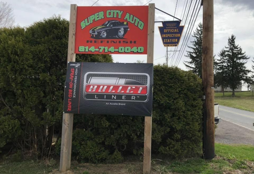 Roadside sign for Super City Auto and KULLER INC., with phone number, beside trees and a road.