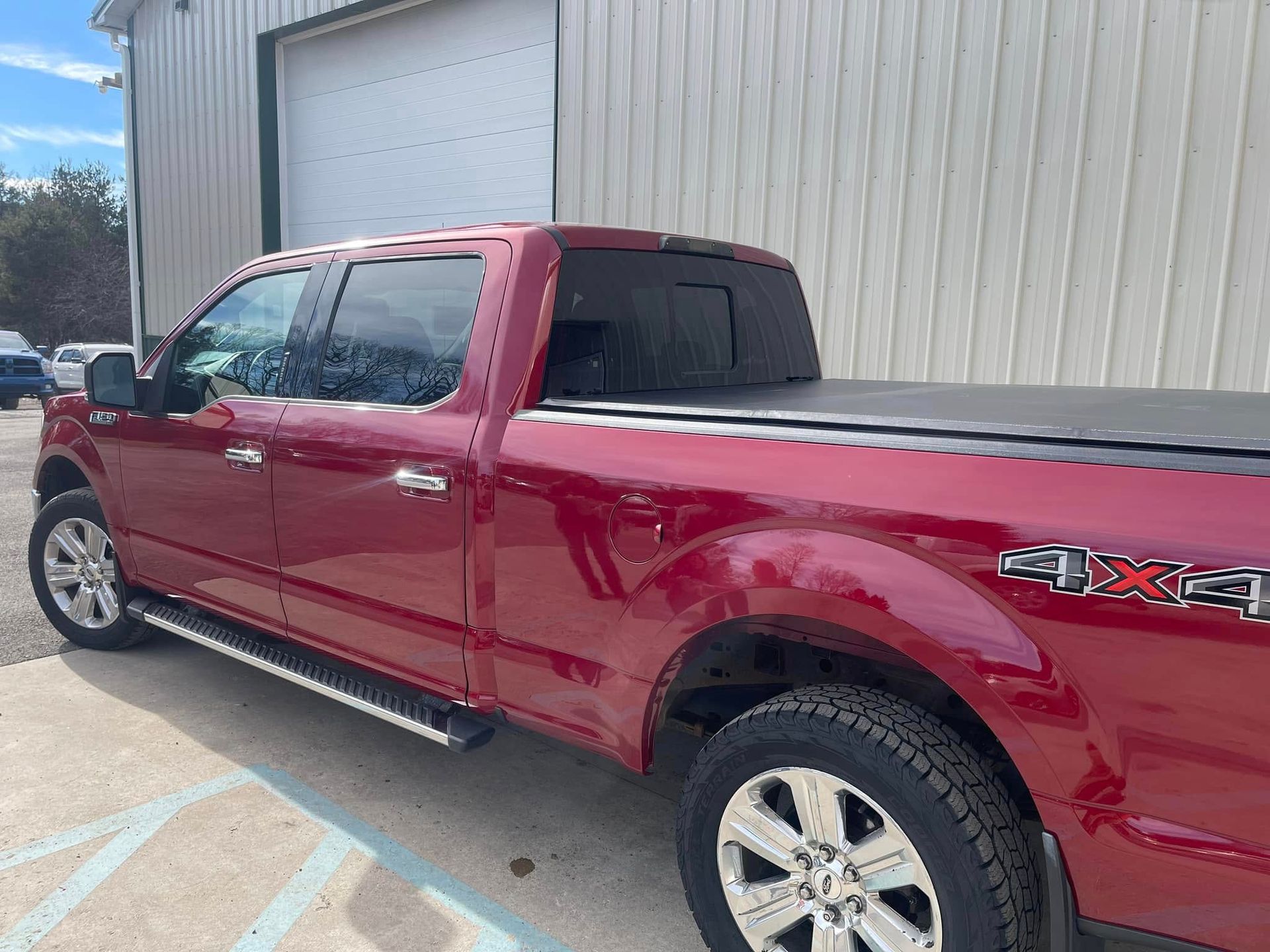 Red pickup truck parked beside a metal building on a sunny day