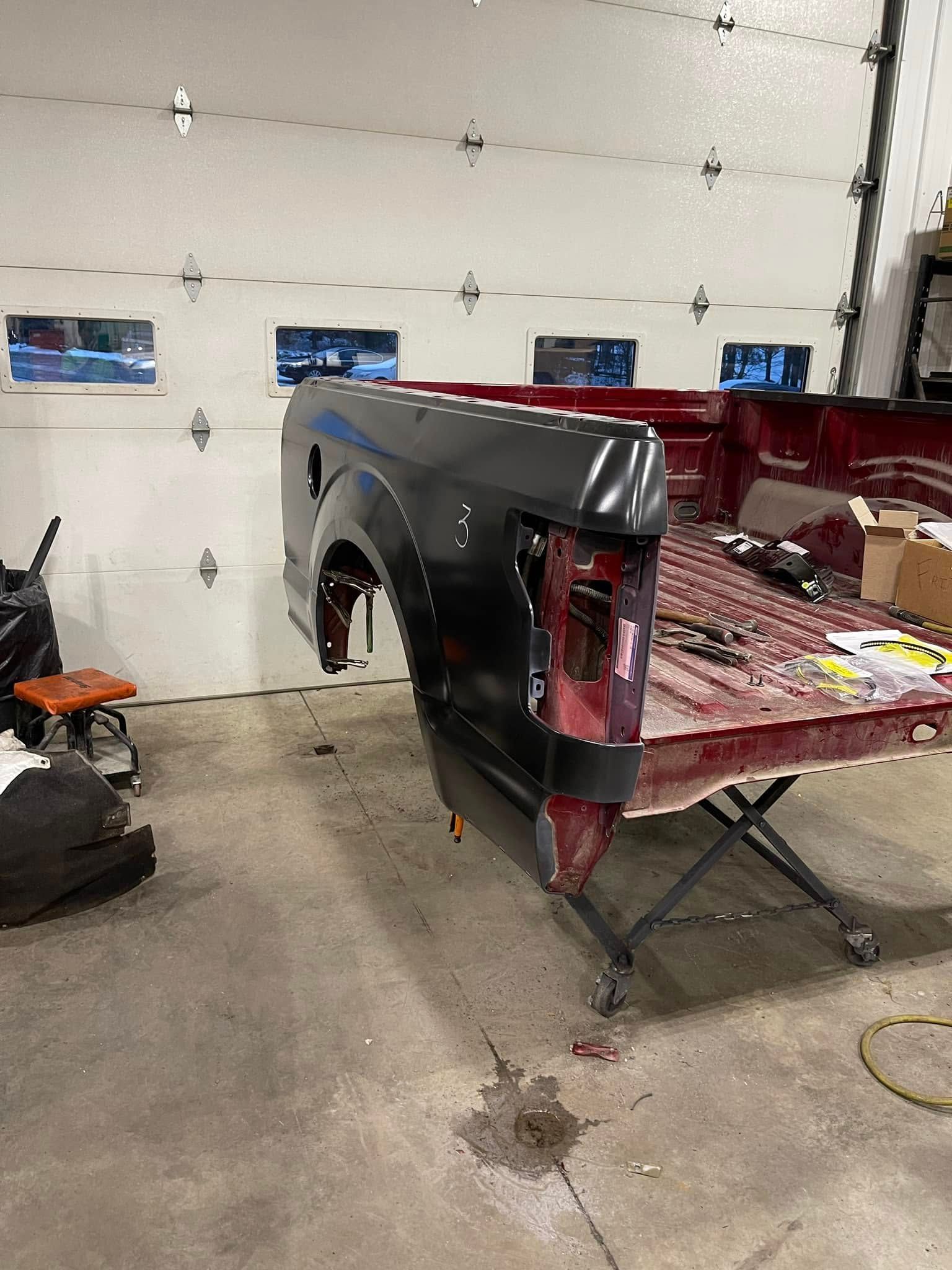 Black pickup truck bed panel in a garage, with red inner bed exposed and garage door behind it