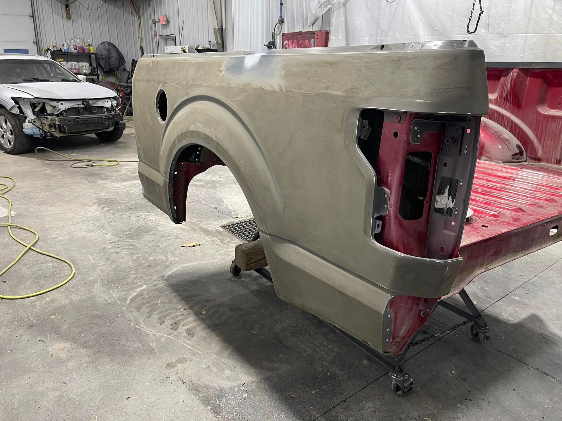 Partially painted truck bed on a wheeled stand in an auto body shop