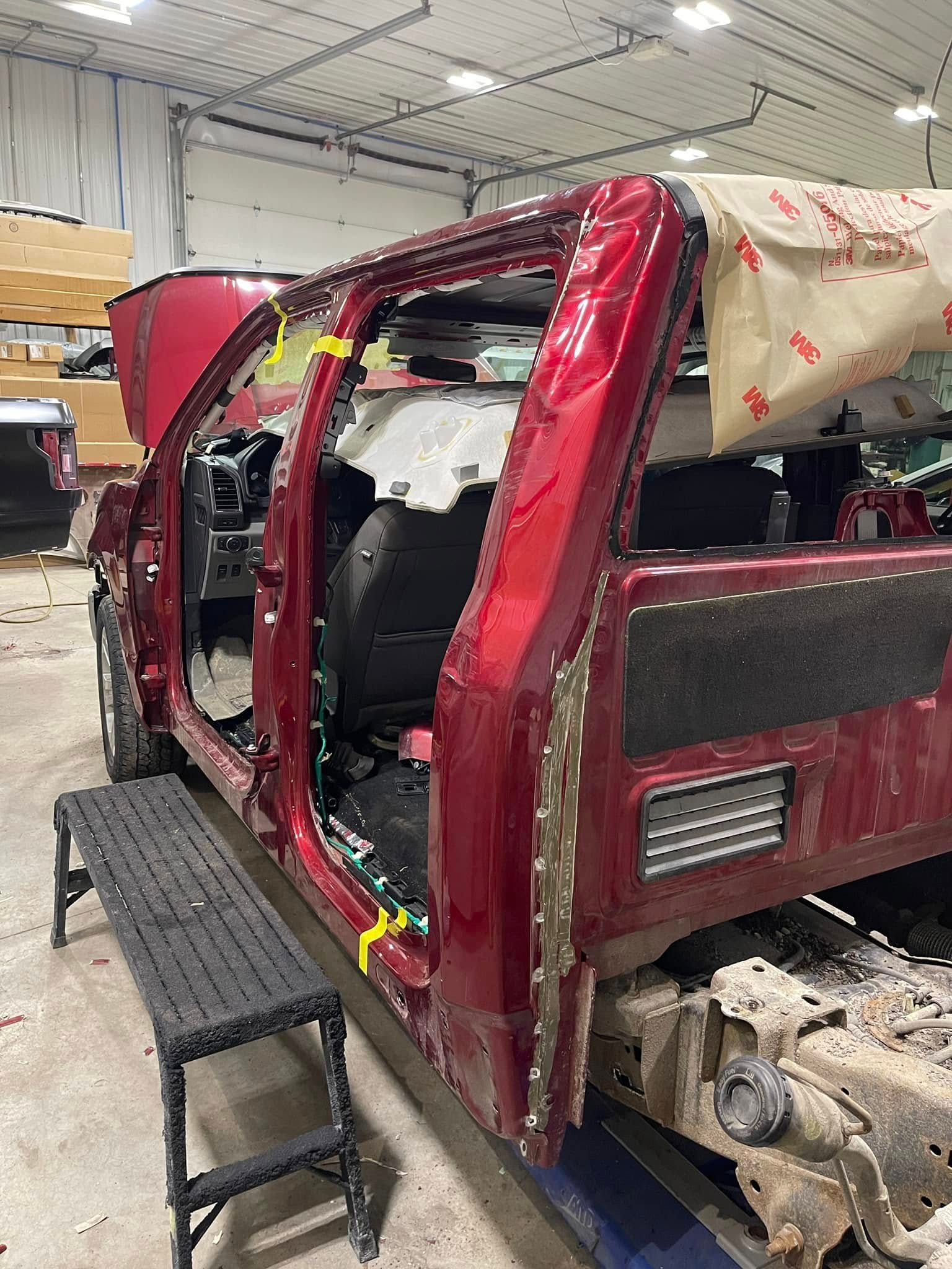 Damaged red pickup truck body in an auto repair shop, with panels removed and interior exposed