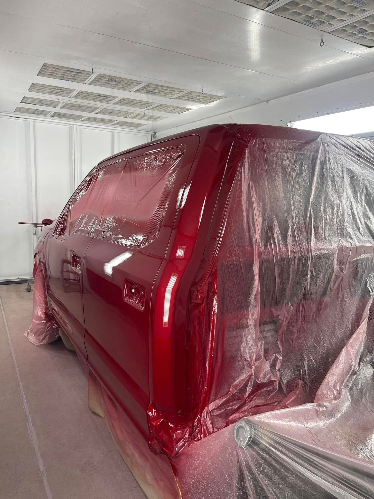 Red car masked with plastic in a paint booth, viewed from the rear side