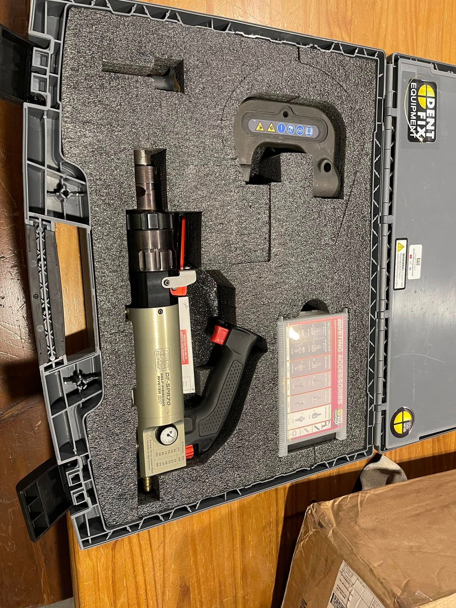 Open equipment case with a flashlight, cable, and labeled compartments on a wooden table.