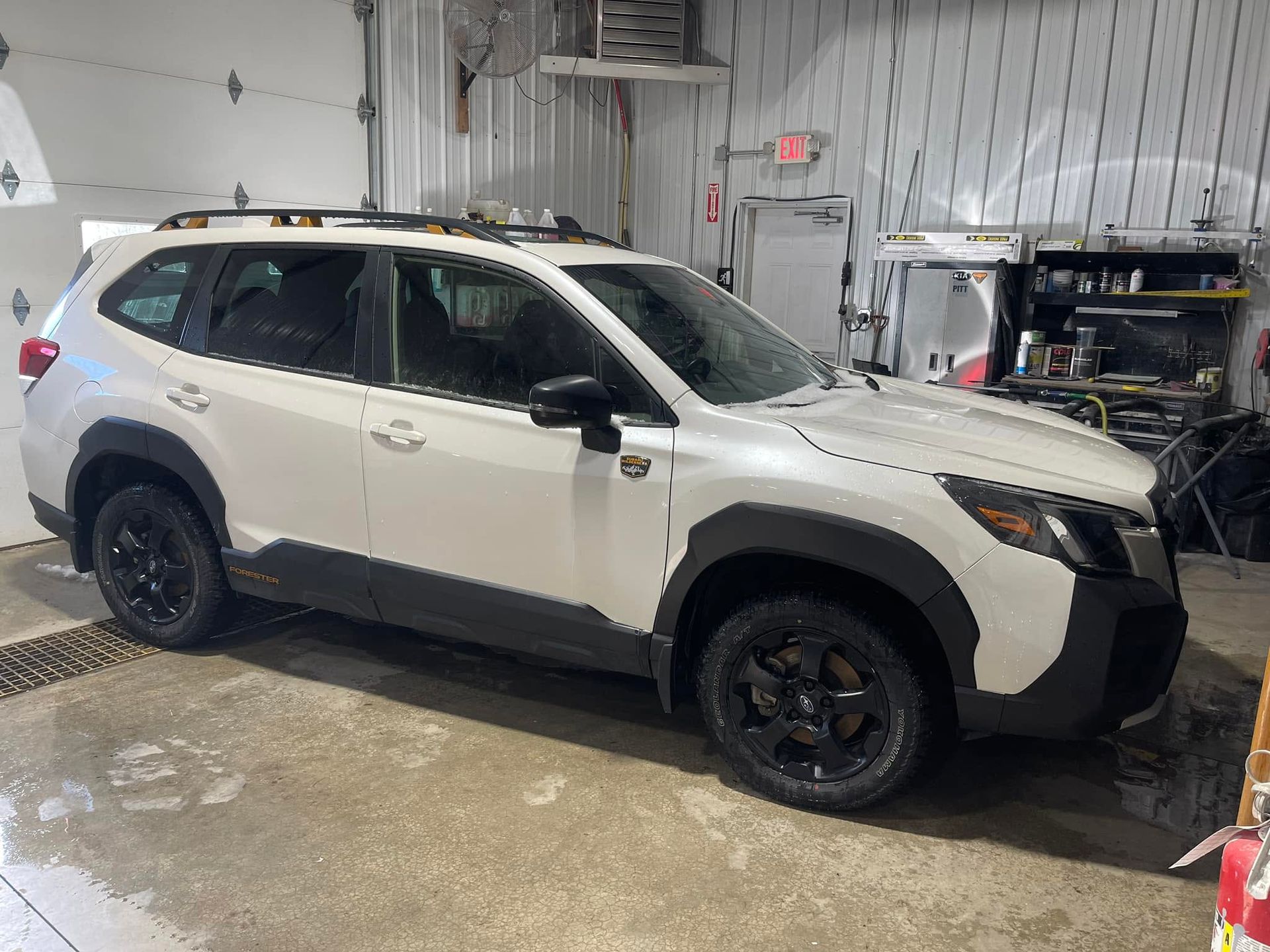 White SUV parked inside an auto shop, with wet floor and tools in the background.