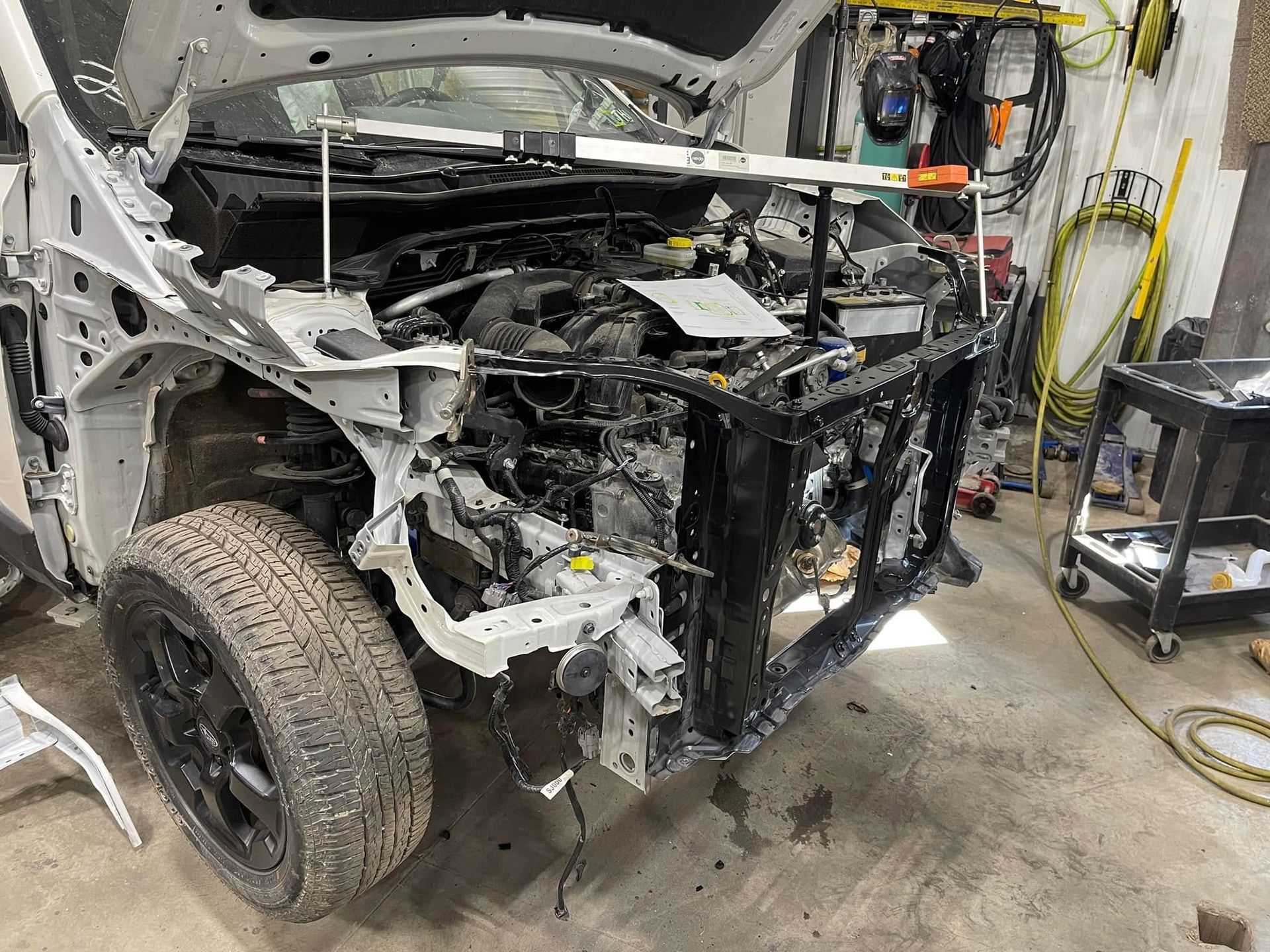 Damaged white SUV with front end removed in an auto repair shop, exposed engine and frame