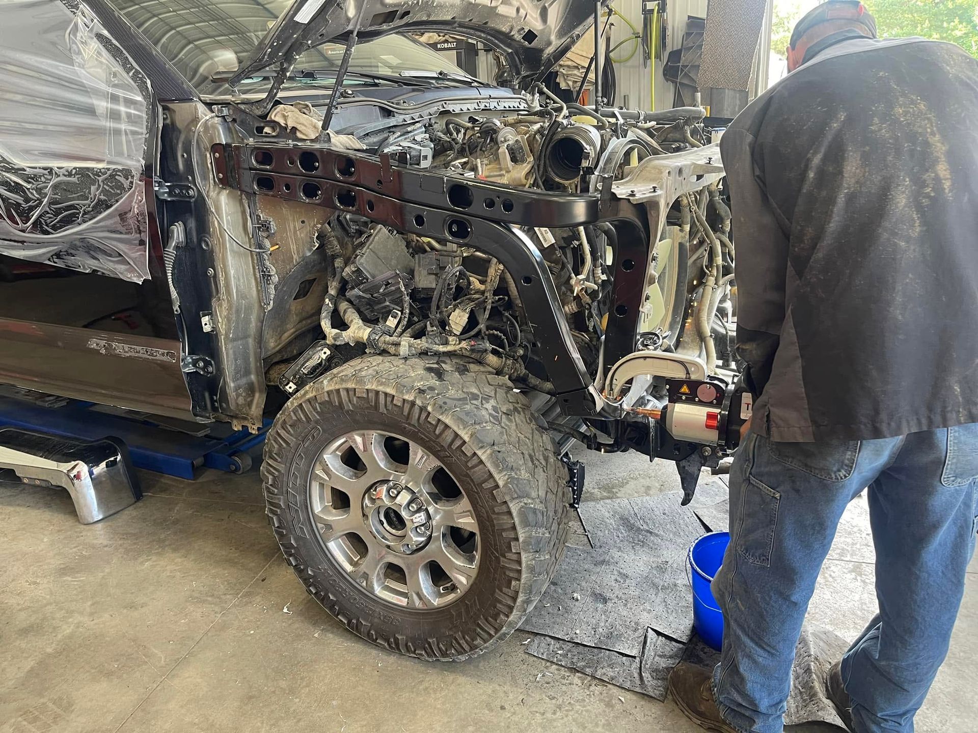 Mechanic working on a damaged off-road vehicle in a garage, with exposed engine and front end removed