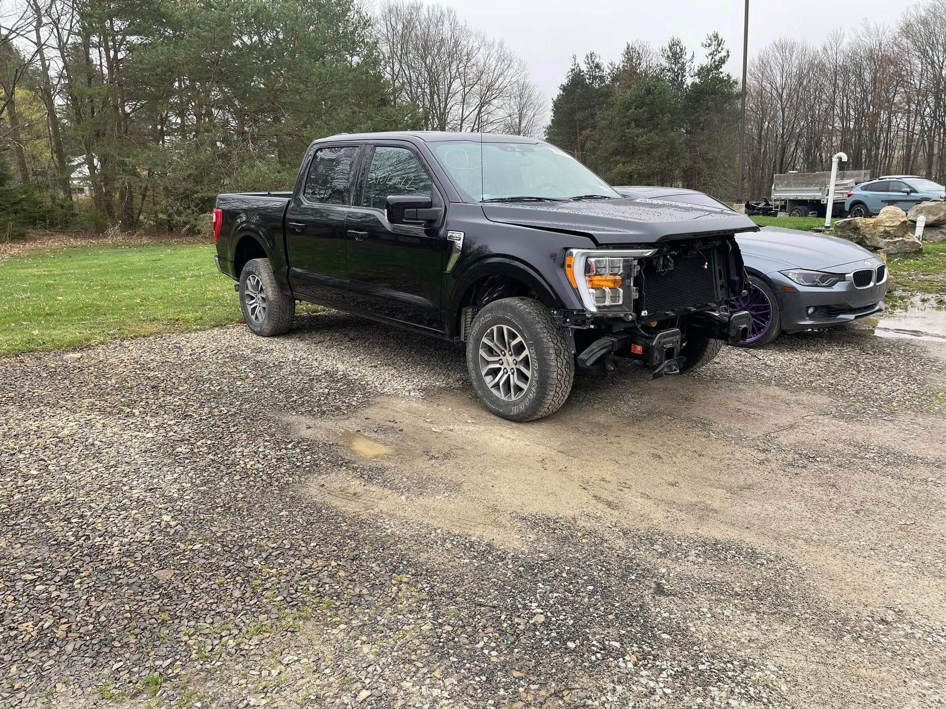 Black pickup with front-end damage after collision with gray car in a muddy lot