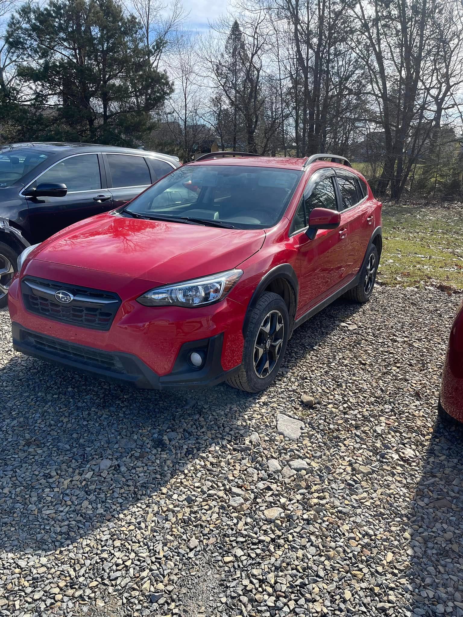 Red SUV parked on a gravel lot with trees and another car in the background.