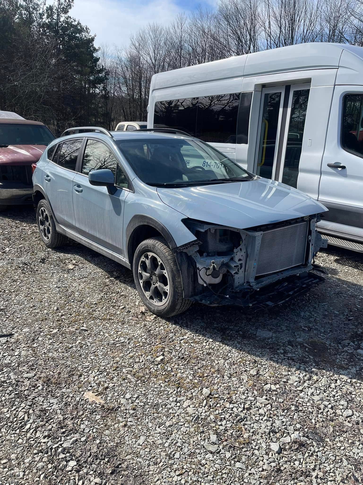Damaged silver SUV parked beside a white RV on a gravel lot, front bumper missing