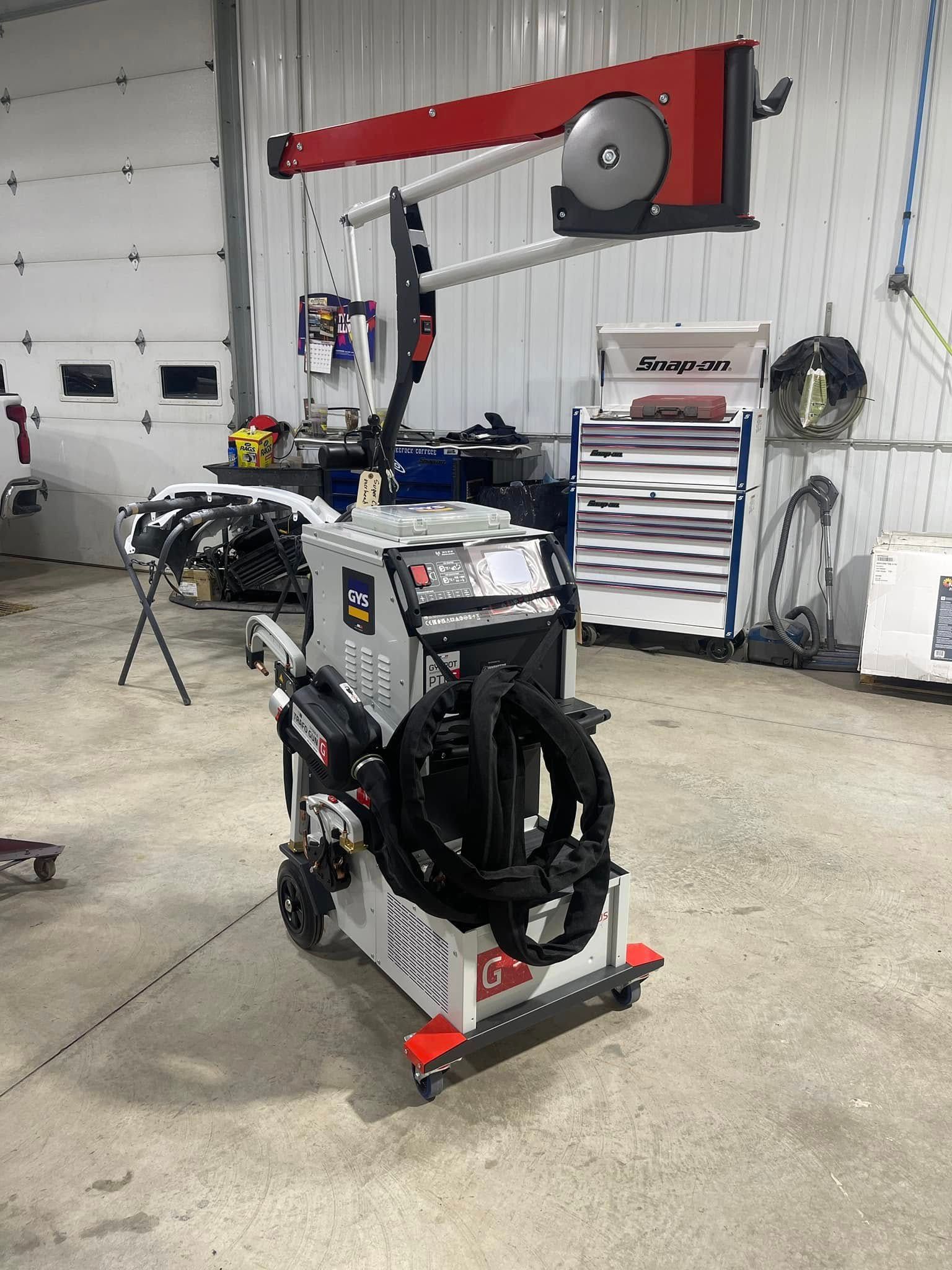 Portable welding machine on a shop floor with coiled hoses and a red overhead hose reel on the wall.