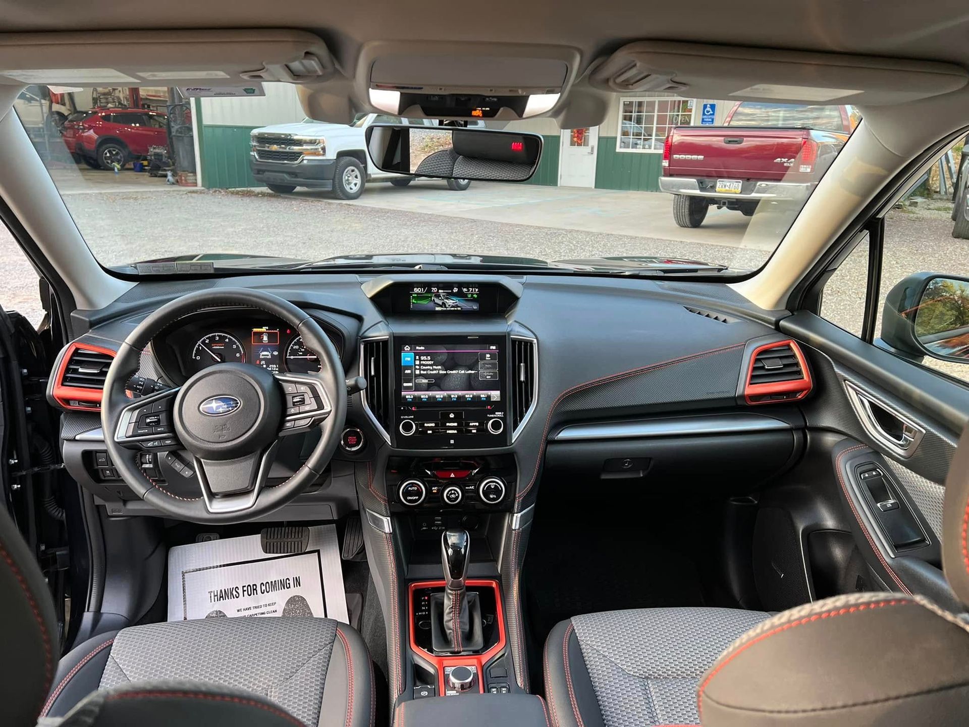 Car interior view with black and red dashboard, steering wheel, and center console, parked outside