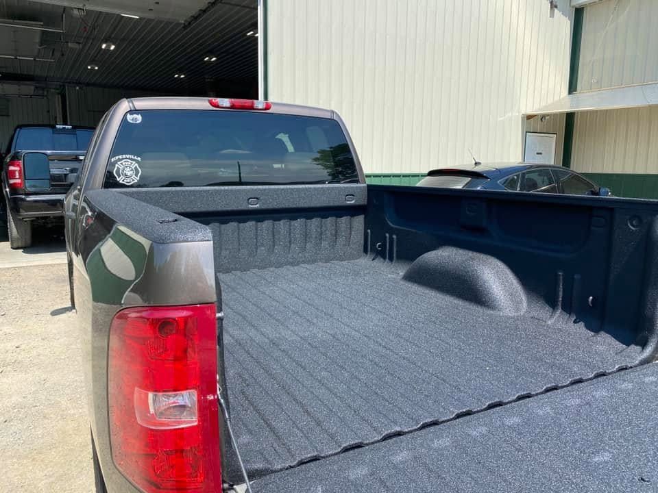 Black pickup truck with tinted rear window and open empty bed parked outside a warehouse.