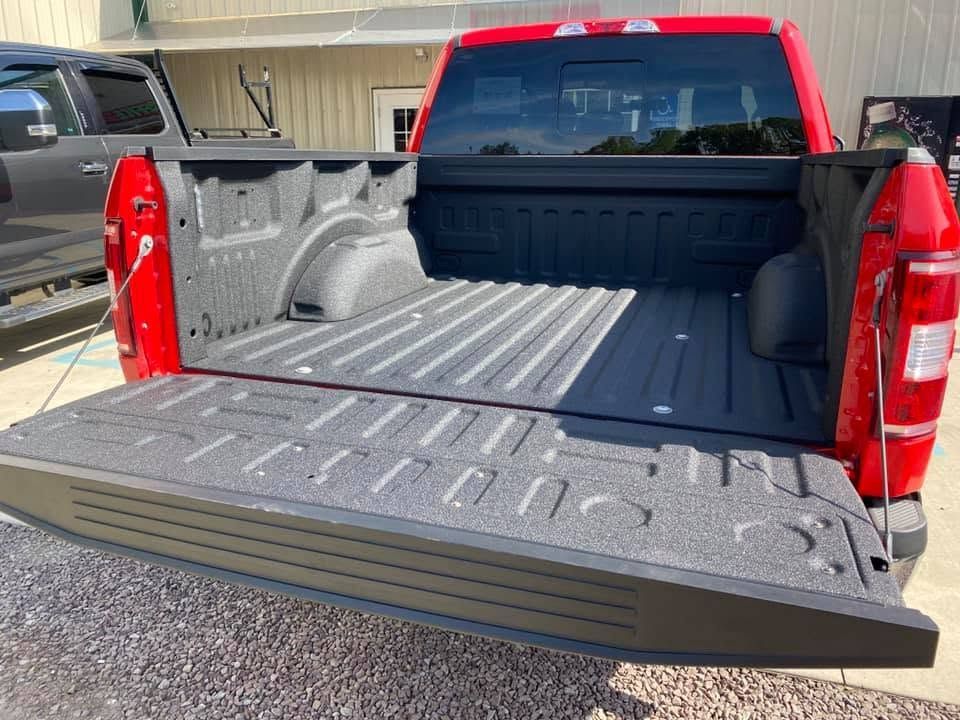 Open pickup truck bed with red cab and tailgate lowered in a driveway