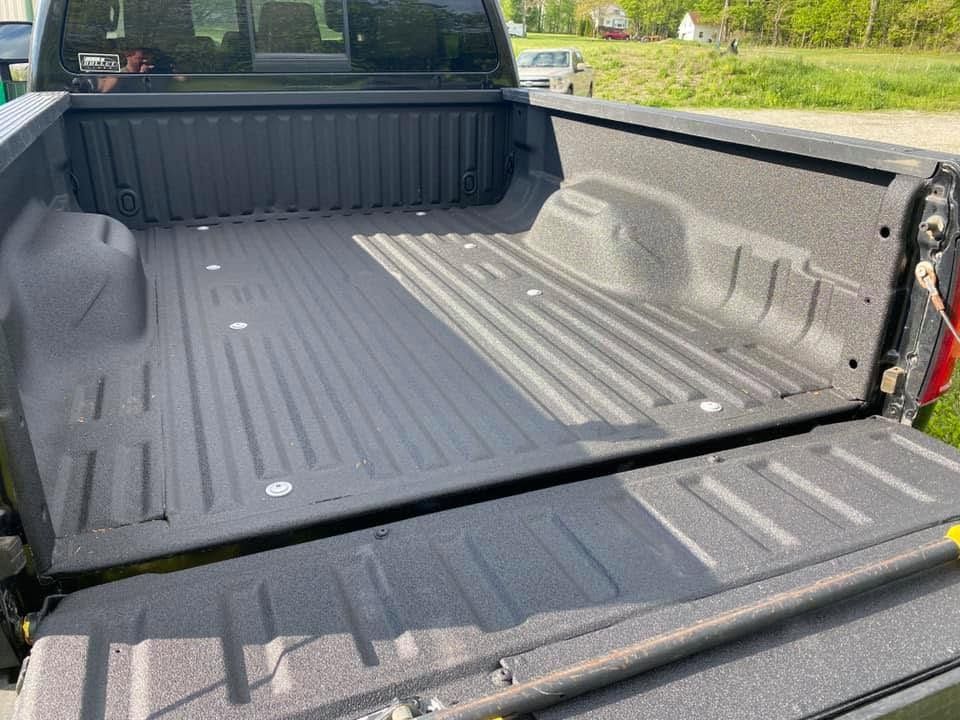 Open pickup truck bed with a black bed liner, viewed from the tailgate.
