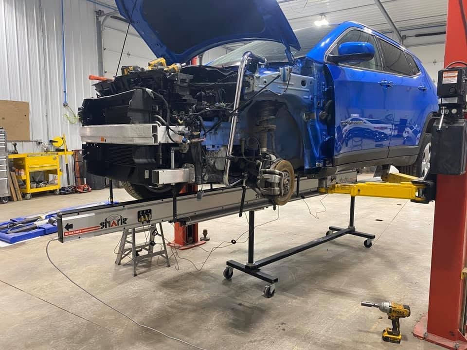 Blue car body on a lift in an auto repair shop, front end disassembled for repair