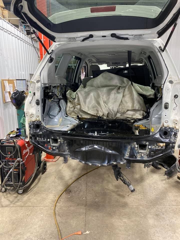 SUV in an auto body shop with the rear removed and interior covered by a tarp, on a jack stand.