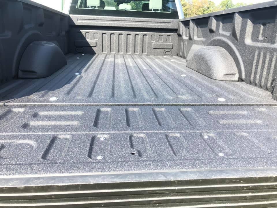 Empty black pickup truck bed with textured liner and tailgate open outdoors