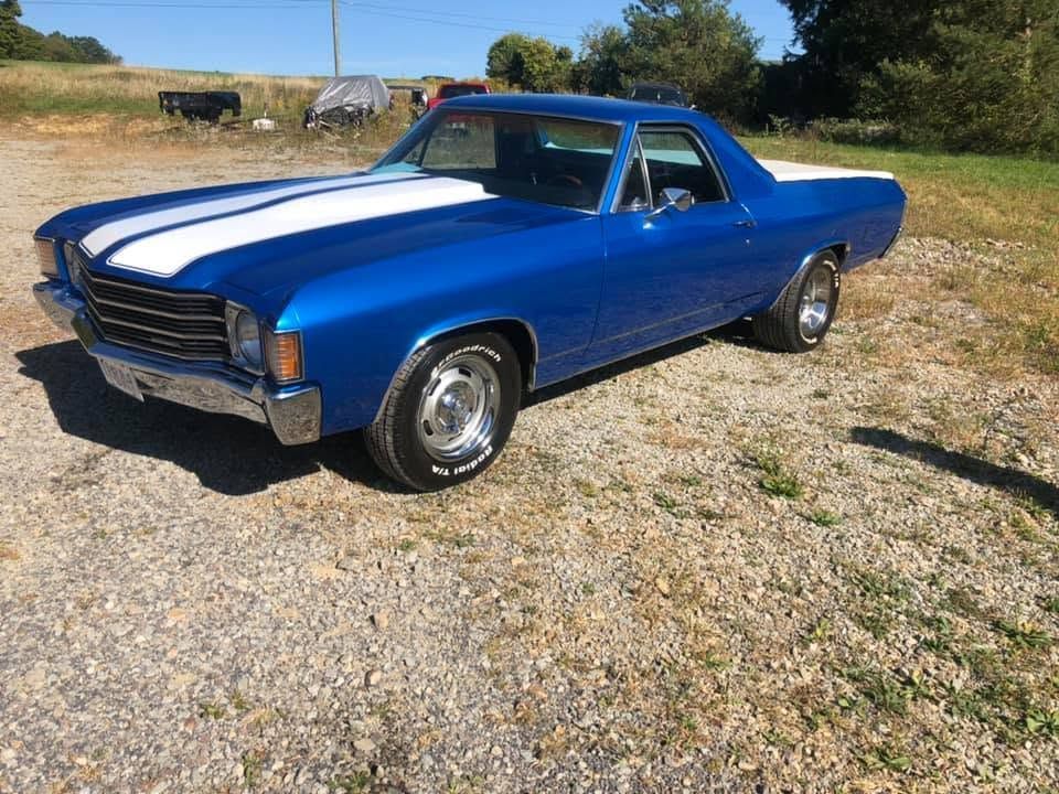 Blue classic car parked on gravel in a sunny rural field