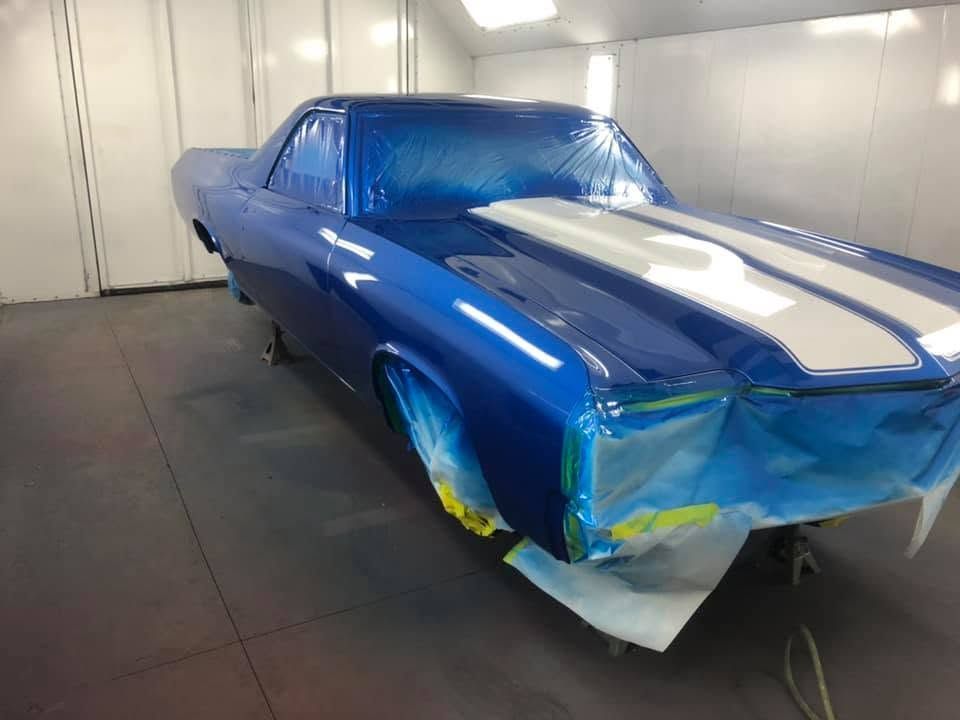 Blue classic car in a paint booth, masked with plastic and tape for repainting.