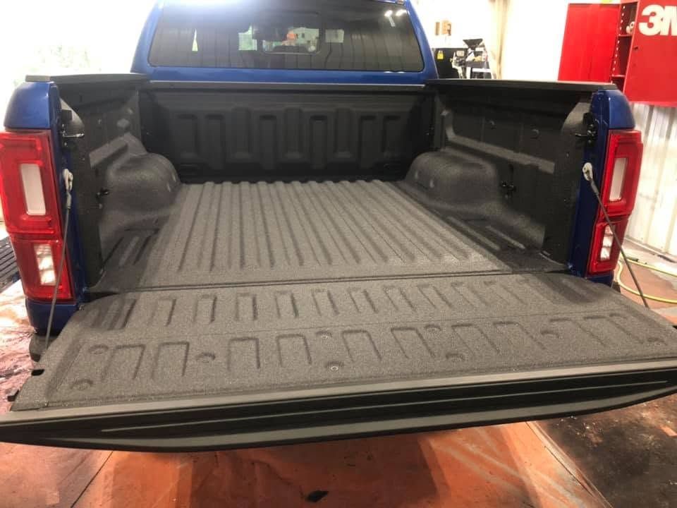 Open truck bed with black liner, viewed from the tailgate in a garage.