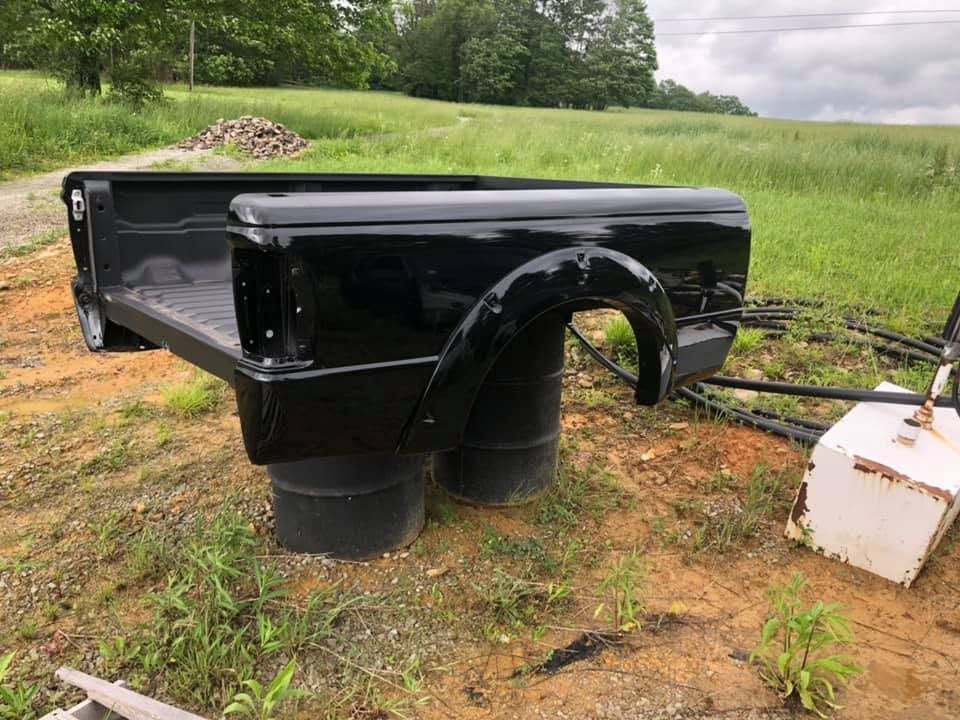 Glossy black truck bed liner on supports in a grassy field, with a white container beside it