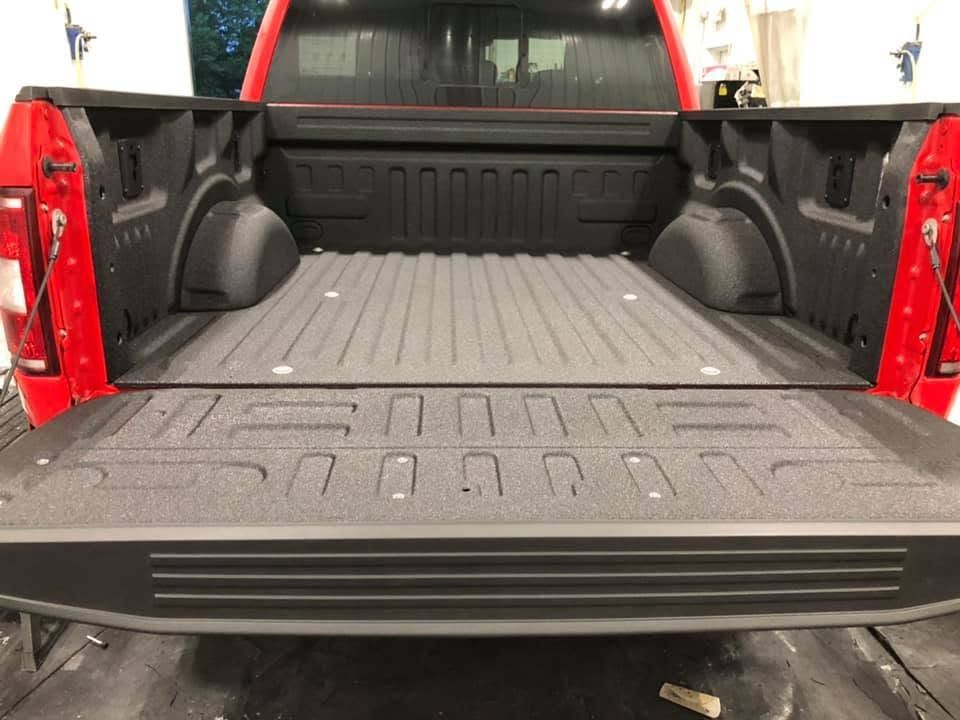 Open pickup truck bed with black liner and red tailgate, viewed from the rear.