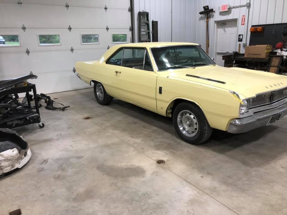 Yellow classic car in a garage beside a disassembled frame and tools