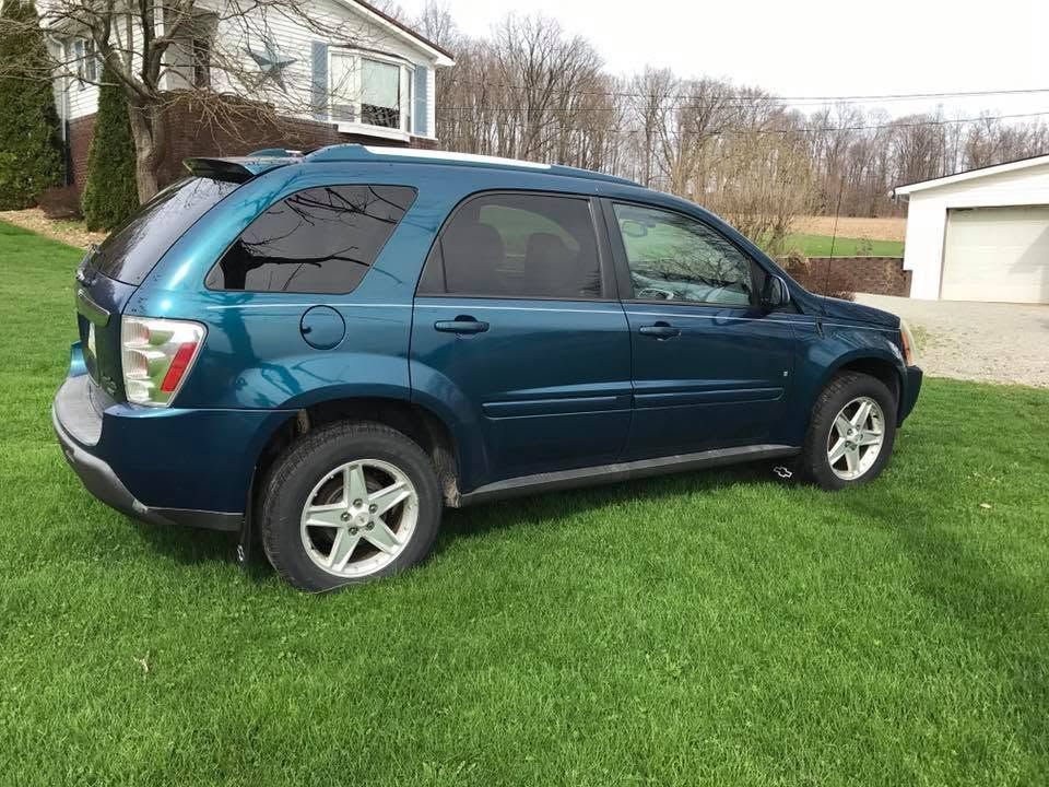 Blue SUV parked on a grassy driveway beside a house and garage.