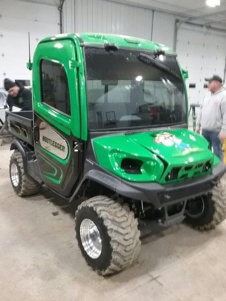 Green off-road utility vehicle indoors, with large tires and a black cab panel.