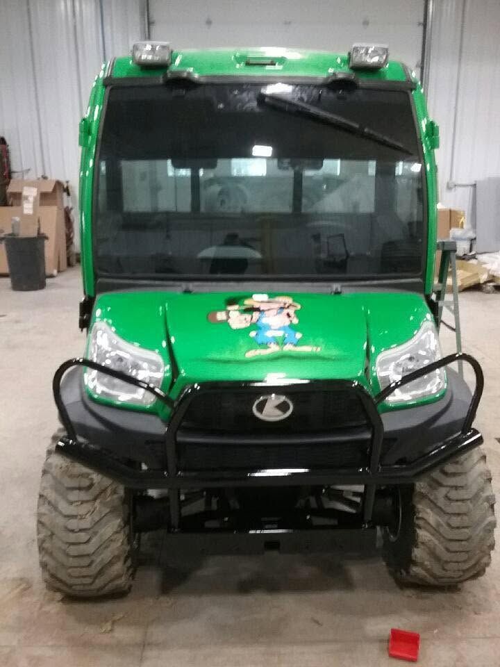 Green utility vehicle in a garage, viewed from the front with large off-road tires.