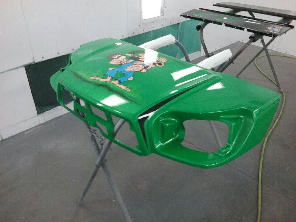 Green car body shell on metal stands in a workshop, with tools on top and a black panel leaning nearby.