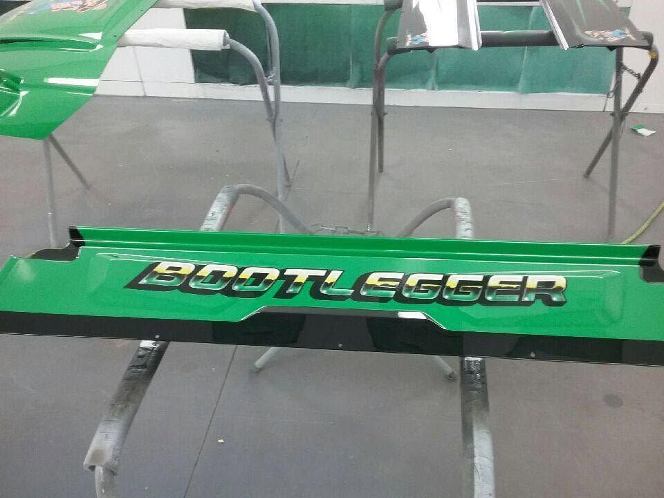 Green rowing shell with the word “Boatslayer” on a gray floor, with metal stands nearby