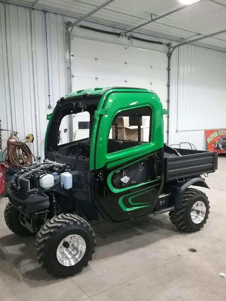 Green and black compact utility truck in a workshop garage, shown from the front-left side.