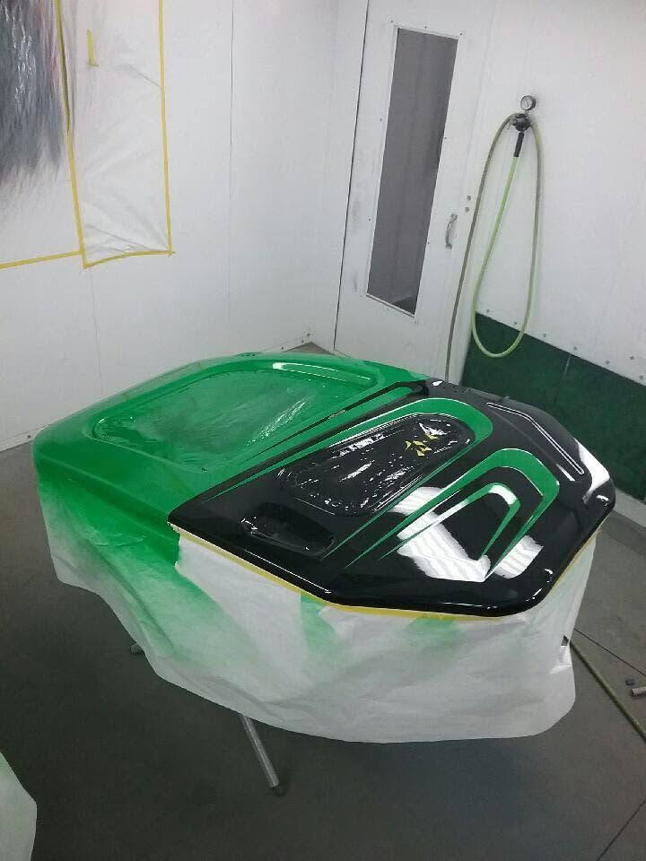 Green and black car part masked for spray painting in a workshop booth