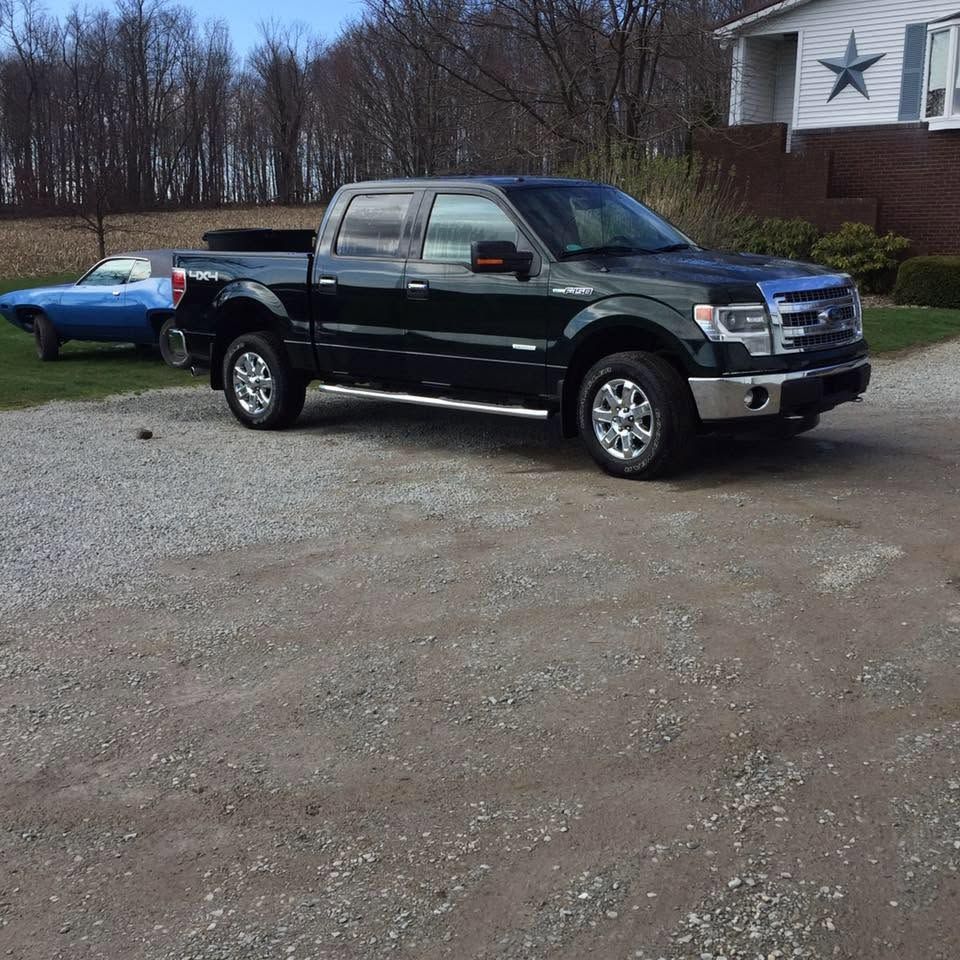 Black pickup truck parked on a gravel driveway beside a blue car and a house.