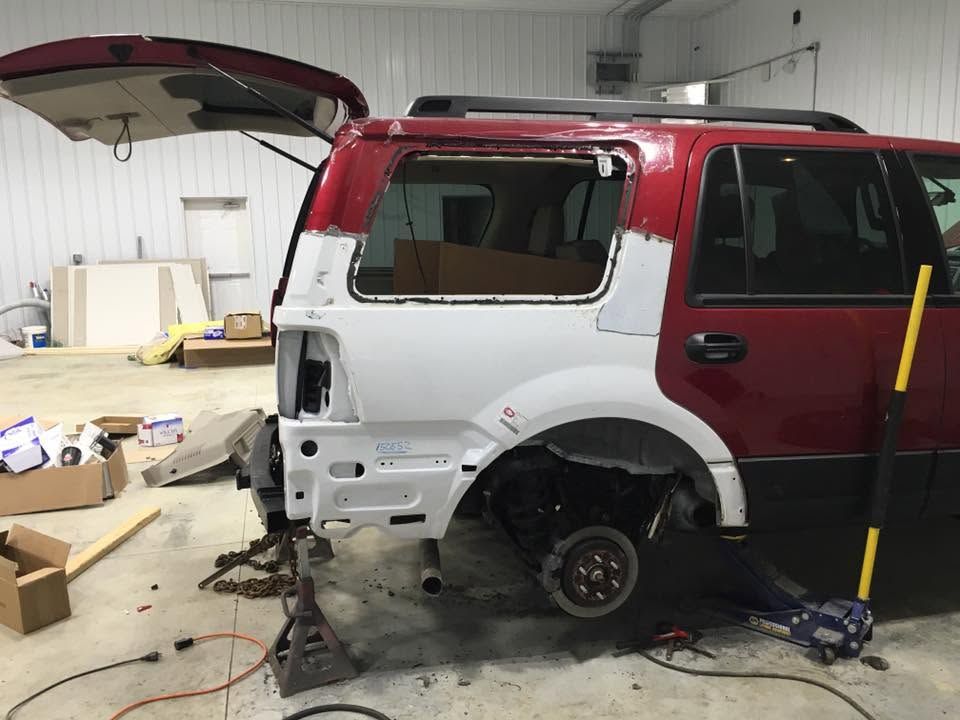 Red and white SUV under repair in a garage, rear side panel removed and wheel off.