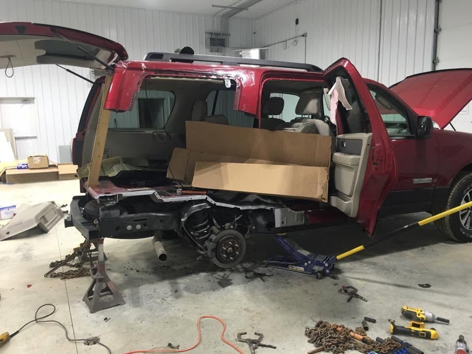 Red SUV with rear damage in a garage, parts removed and tools scattered on the floor.