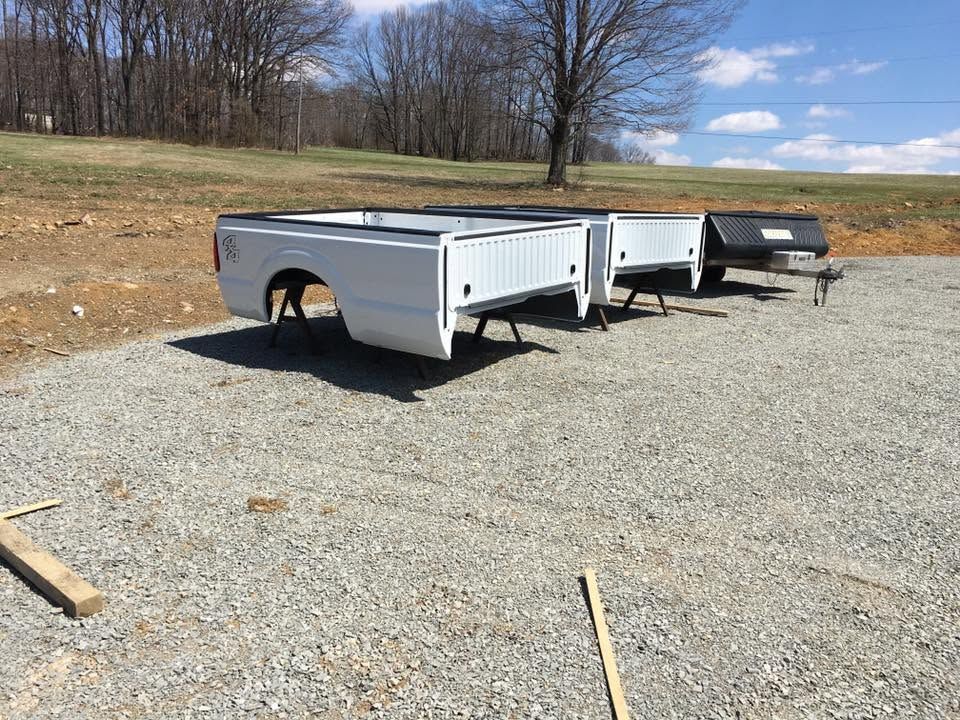 Three utility trailers parked on gravel in a grassy lot under a cloudy sky