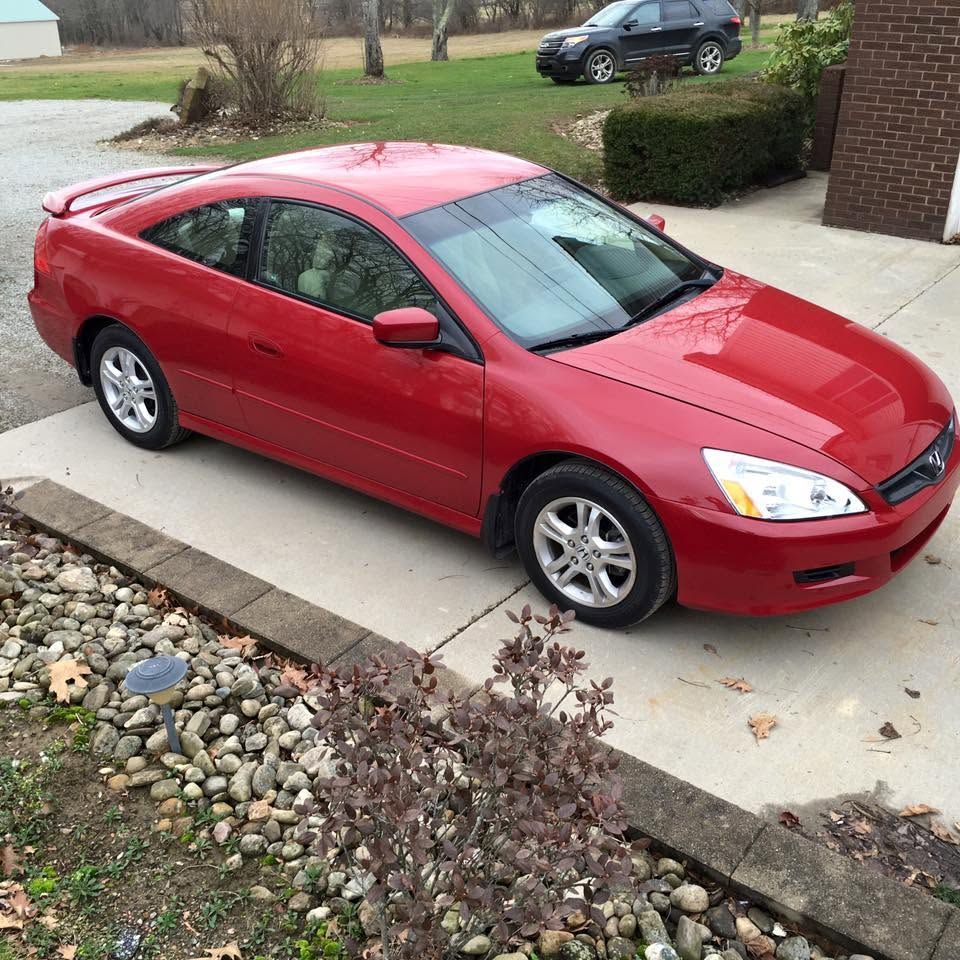 Red coupe parked in a driveway beside a house, with a landscaped front yard.