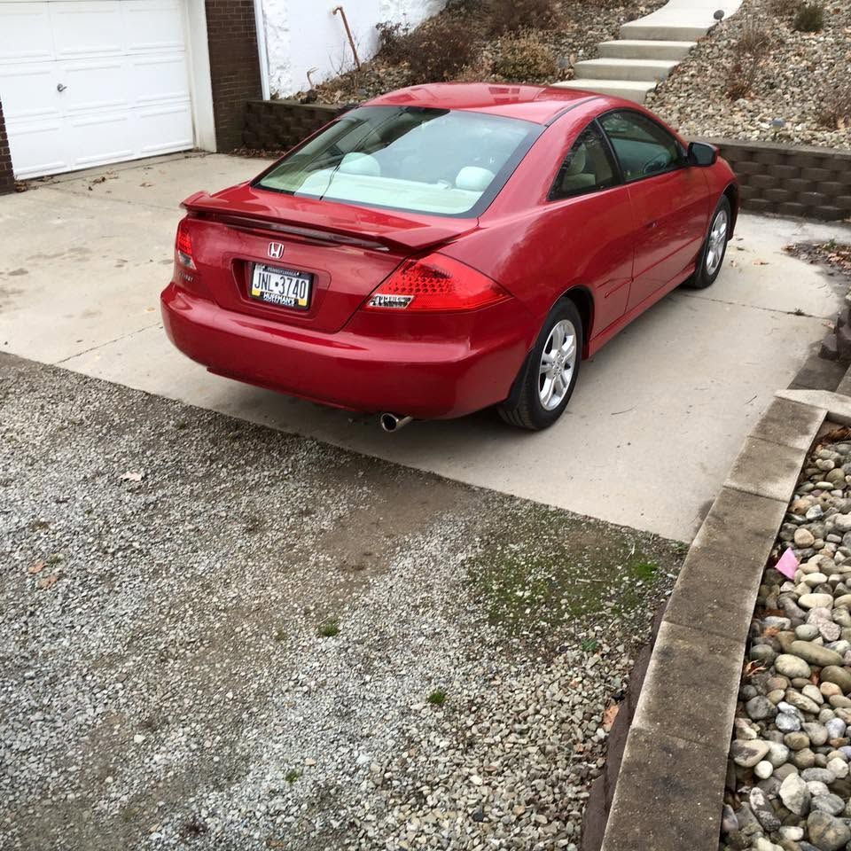 Red two-door coupe parked on a driveway beside a house and gravel yard