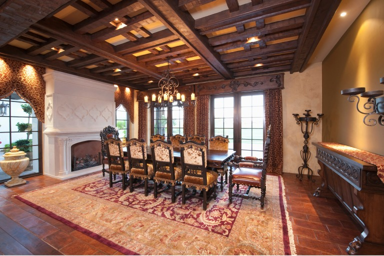 Formal dining room with dark wood ceiling beams, ornate table and chairs, fireplace.