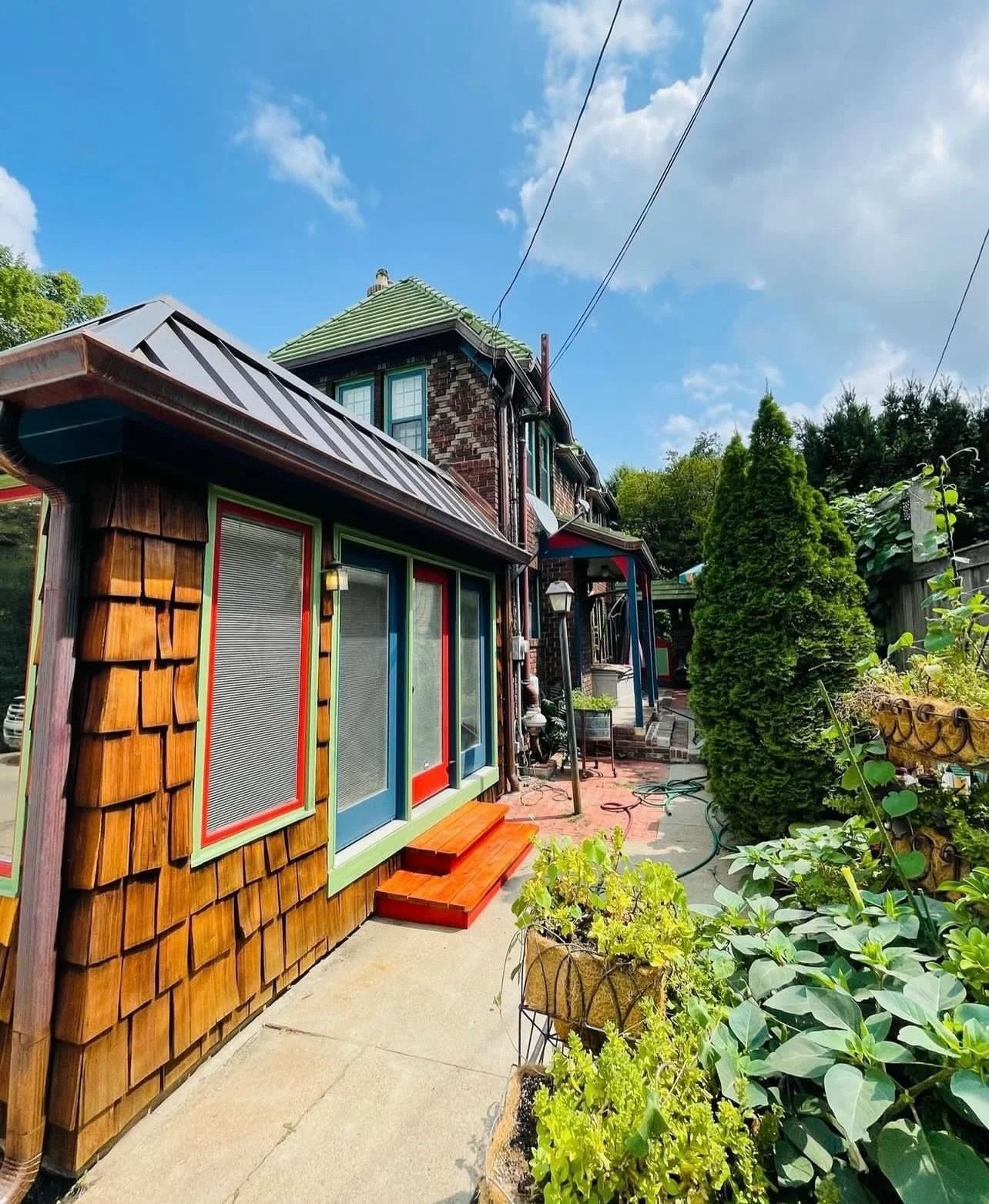 A colorful house with wooden shingles, red steps, and a lush garden path.